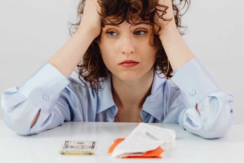 Imagem Ilustrativa - Há uma moça de cabelo cacheado. Ela está preocupada com a mão na cabeça.